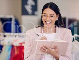 Nothing feels better than being fully booked. Shot of an attractive young seamstress writing notes while working in her boutique.