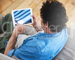 Wifi all weekend long. Rearview shot of a bachelor relaxing on the sofa with his tablet.