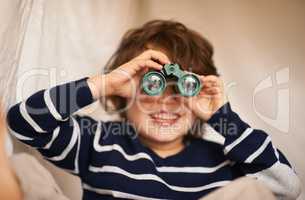 Lets see what mischief I can get up to today. Shot of an adorable little boy playing with a pair of binoculars.