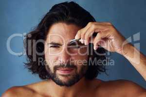 Giving his brows some defined shape. Studio portrait of a handsome young man plucking his eyebrows against a blue background.