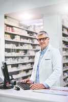 So many meds to choose from. Portrait of a confident mature male pharmacist typing on a computer while looking at the camera in the pharmacy.