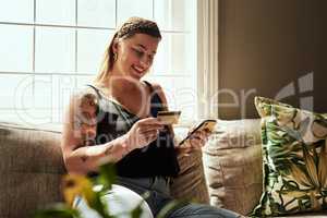 Shopping day minus the queues. Shot of a young woman using a smartphone and credit card on the sofa at home.