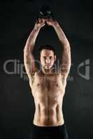 Raise your game. Studio portrait of a shirtless young man working out with a kettle bell against a dark background.