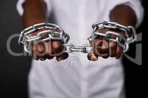 Whats holding you back in life. Cropped shot of a mans hands tied up with chains against a black background.