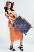 Im packed for my vacation. Studio shot of a beautiful young woman holding up her suitcase while standing against a white background.