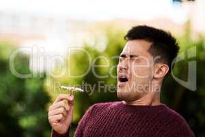 Hayfever season. Cropped shot of a young man sneezing after smelling a flower.