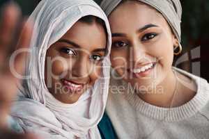 Capture this. Cropped portrait of two affectionate young girlfriends taking a selfie together at a cafe while dressed in hijab.