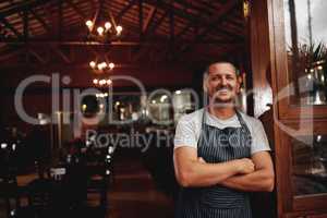 The master taking a break. Portrait of a confident middle aged business owner standing with arms folded under a doorway at a beer brewery during the day.