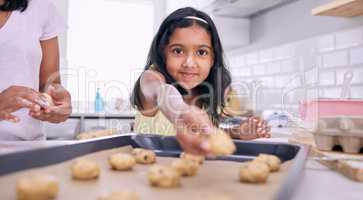 Chocolate chip cookies are my favourite. Shot of an adorable little girl placing cookie dough on a baking tray.