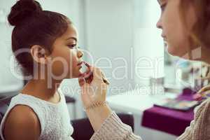 Shes a little pageant princess. Shot of a stylist applying makeup to a cute little girl in a dressing room.