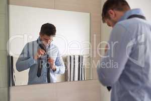 Get up and get dressed for a day of success. Shot of a young man tying his tie in front of the bathroom mirror.