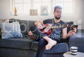 Hes developed a well-tuned musical ear. Cropped shot of a handsome young man playing a guitar at home.