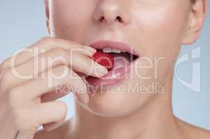 Biting into goodness. Studio shot of an unrecognizable young woman biting into a strawberry against a grey background.