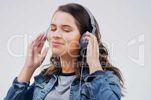 Finding her bliss in the music. Studio shot of an attractive young woman dancing against a grey background.