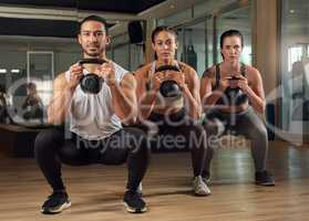 Kettle bells are a great workout. Full length portrait of three young athletes working out with kettle bells in the gym.