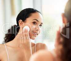 Keep your face clean. Shot of a young woman using a cotton pad to clean her face in a bathroom at home.