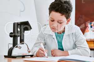 Getting top grades is what he always strives for. Shot of an adorable young school boy writing notes in his note book in science class at school.