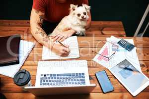 My best friend always wants to cuddle while Im working. High angle shot of an unrecognizable businesswoman sitting with her pet dog and writing in her notebook.