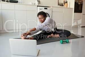 Online training is really growing in popularity. Shot of a young woman using a laptop while exercising at home.