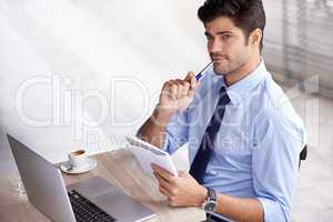Coffee-induced innovation. A handsome young businessman sitting at a cafe with his laptop and a notepad.