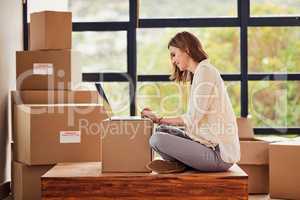 Setting up her forwarding address online. Shot of a young woman using a laptop while taking a break from moving into a new home.