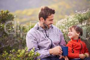 Bonding in the great outdoors. Shot of a happy father and son having something to drink while on a hike together.