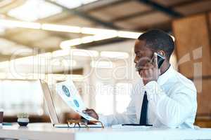 The charts say the same thing. Shot of a focused young businessman talking on his cellphone and looking at a graph while being seated in the office during the day.