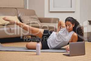 This is harder than it seems. Full length shot of a young woman using her laptop to follow an online fitness class in her living room.