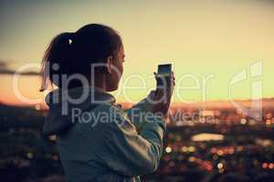 Theres always time for a photo. Rearview shot of a young woman sending a text message while standing on a lookout point.