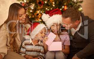 Yuletide joy. A little girl receiving a Christmas present while surrounded by her family.