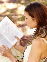 Her weekend is all booked. Shot of an attractive young woman reading a book in the park.
