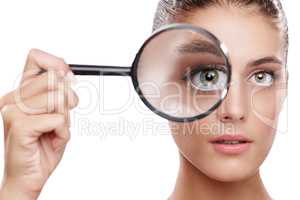 Magnifying her best features. Studio shot of a beautiful woman with a magnifying glass in front of her eye.