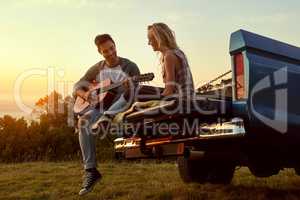 Love and leisure in perfect harmony. Shot of a young man playing guitar for his girlfriend on a roadtrip.