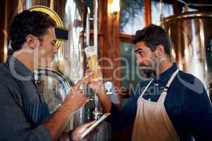 The color of the beer also says a lot about it. Shot of two focused young male business owners testing out a fresh batch of beer inside of their beer brewery during the day.