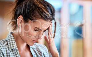 Where did this headache come from all of a sudden. Shot of a uncomfortable looking woman holding her head in discomfort due to pain at home during the day.
