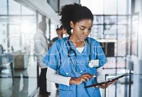 Less paper, more diagnosis. Shot of a young doctor using a digital tablet in a hospital with her colleagues in the background.