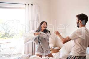 Start every morning with silliness. Shot of a happy young couple having a pillow fight in bed.