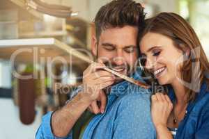 Nurturing their marriage with tasty and nutritious food. Shot of a man giving his wife a taste of the food that hes preparing at home.