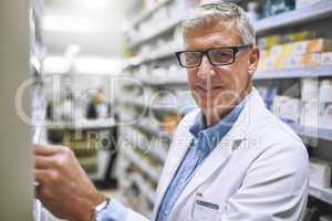 Stocking up on some new meds. Portrait of a cheerful mature male pharmacist getting medication from a shelf while looking at the camera in a pharmacy.