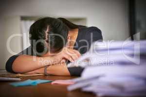 Stuck in a perpetual paperwork nightmare. Shot of an unidentifiable businesswoman lying on her arms next to a pile of paperwork in the office.