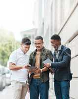 Doing business minus the desk. Shot of a group young businessmen using a digital tablet together against an urban background.