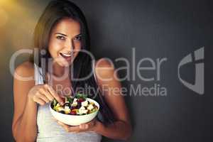 Does the body good. Portrait of a healthy young woman eating a salad against a gray background.