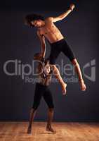 Power to help him fly. Two male contemporary dancers performing a dramatic pose in front of a dark background.