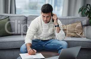 Part living space, part work space. Shot of a young man using a laptop and smartphone while writing in a notebook at home.