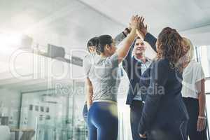 United in their quest for success. Shot of a diverse group of coworkers high fiving together in an office.