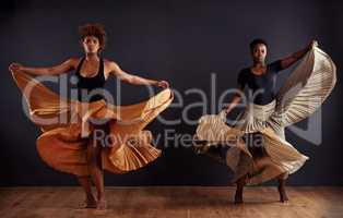 Feminine freedom. Two contemporary dancers with flowing skirts in front of a dark background.
