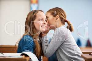 Promise you wont tell anyone.... Shot of an elementary school girl whispering in her friends ear in class.