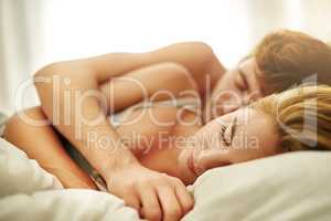 Wrapped in a safe cocoon of marital bliss. Shot of a young couple asleep in bed at home.