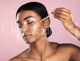 Her skin will be the envy of all. Studio shot of a beautiful young woman applying essential oil to her face with a dropper posing against a pink background.