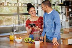 Downloading a dieting app designed for couples. Shot of a happy young couple using a digital tablet while preparing a healthy snack together at home.